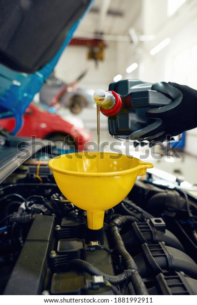 Man\
pouring engine oil into car motor through funnel at car service\
station, vertical shot. Auto repairing\
concept