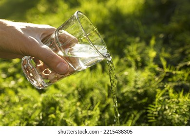 Man Pouring Fresh Water From Glass Outdoors, Closeup