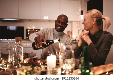 Man pouring a friend a glass of wine during a candlelit dinner party around a table with friends 