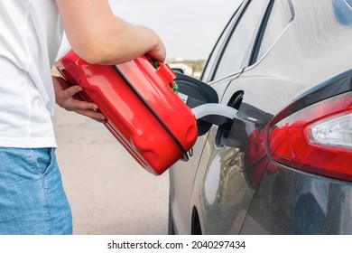 A Man Pouring Gasoline Into An Empty Fuel Tank From A Plastic Red  Gas Can. Filling  The Car From The Canister Into The Neck Of The Fuel Tank. 