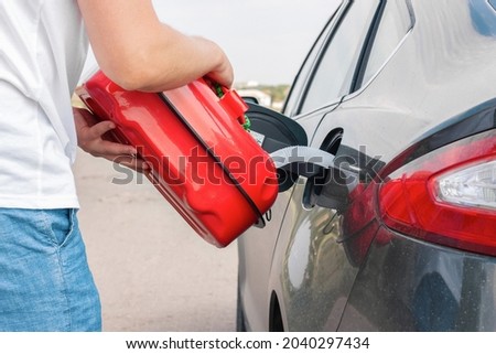 A man pouring gasoline into an empty fuel tank from a plastic red  gas can. Filling  the car from the canister into the neck of the fuel tank. 