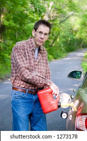 A Man Pouring Gasoline Into The Gas Tank Of His Car From  A Red Gas Can.  He's Standing On A Country Road In The  Middle Of Nowhere, Lost.