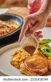 A Man Pouring Gravy Sauce On Pork Steak With Green Salad