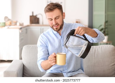 Man Pouring Hot Boiled Water From Electric Kettle Into Cup At Home