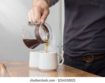 The man is pouring hot coffee from the coffee pot into the white coffee on the wooden table in the morning - Powered by Shutterstock