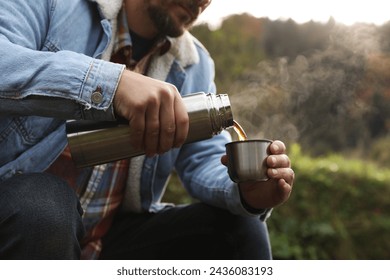 Man pouring hot drink from metallic thermos into cup lid in nature, closeup - Powered by Shutterstock