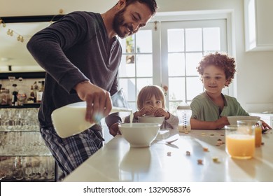 Man pouring milk in to bowls for breakfast at home. Father and kids having breakfast at home. - Powered by Shutterstock