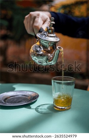 Man pouring mint tea, close up. Silver oriental teapot kettle and tea cup glass to drink traditional moroccan tea in local Riad. Morocco, Africa