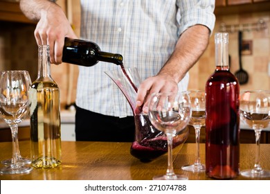 Man Pouring Red Wine From Bottle Into A Decanter, Home Kitchen Interior, Bottles Of Wine