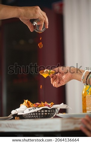 Man pouring spicy red tomato sauce on mexican snack nacho in a restaurant