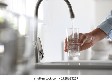 Hombre vertiendo agua en vidrio en la cocina, en el armario