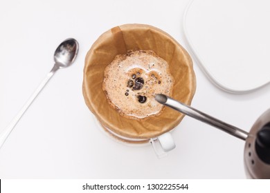 Man pouring water from the kettle into the coffee filter. Fresh morning pour over coffee blossoms in the dripper. Brewing coffee alternative method in pour over, top view on white background - Shutterstock ID 1302225544