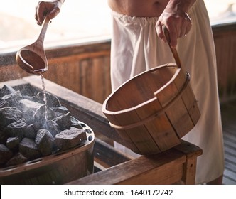 Man pouring water onto hot stone in sauna room. Steam on the stones, spa and wellness concept, relax in hot finnish sauna.