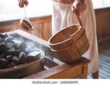 Man pouring water onto hot stone in sauna room. Steam on the stones, spa and wellness concept, relax in hot finnish sauna.