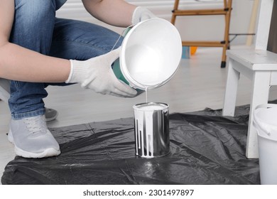 Man pouring white paint from bucket into can indoors, closeup
