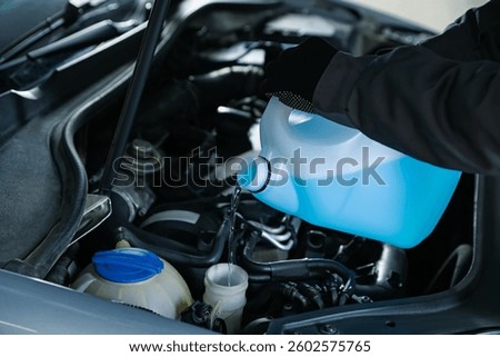 Man pouring windshield washer from plastic canister into car reservoir, closeup