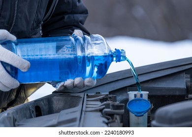 A man pours blue glass cleaner from a bottle into a car window washer tank. - Shutterstock ID 2240180993