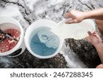 A man pours creamy clear shampoo to a pail of water, getting ready for a car wash at an auto detailing shop.