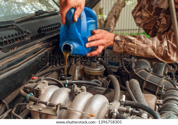 A
man pours oil into the car engine. car engine and oil canister.
human hands and oil change in a car. Car
maintenance.