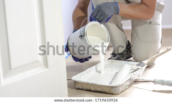 Man pours paint into the tray and dips roller.\
Professional interior construction worker pouring white color paint\
to tray.