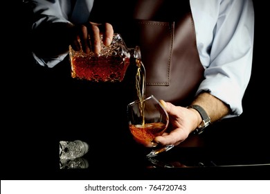 the man pours some brandy into a glass behind the bar