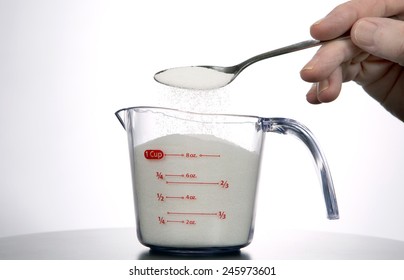 Man Pours A Spoonful Of Sugar Into A Measuring Cup.