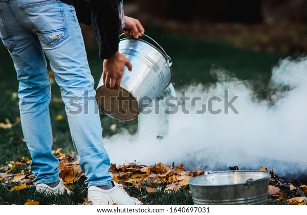 man pours water from a bucket a bonfire\
on the grass. protect the forest from\
fire