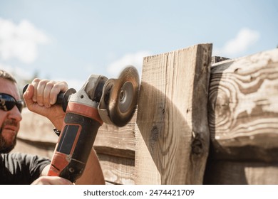 A man with a powerful tool with an angle grinder cleans the wood of the fence - grinding the boards with a coarse grinder brush - Powered by Shutterstock