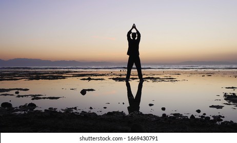 Man practices qigong exercises, shallow water reflecting figure.