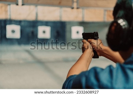 A man practices shooting a pistol in a shooting range while wearing protective headphones