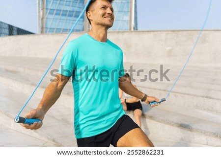 Man practices skipping rope exercise outdoors in bright sunlight near modern building