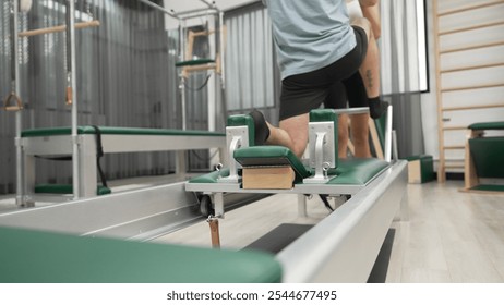 Man practicing kneeling stretch on pilates reformer with assistance to improve flexibility and strength. Trainer assist student doing lunge stretch on the reformer for enhancing balance. Habituate. - Powered by Shutterstock