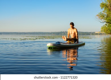 Man practicing yoga on a SUP board during sunrise on a large river. Stand up paddle boarding - awesome active recreation in nature.