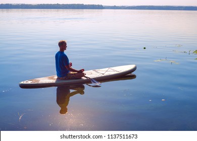 Man practicing yoga on a SUP board during sunny morning on a large river. Stand up paddle boarding - awesome active recreation in nature. Backlight.