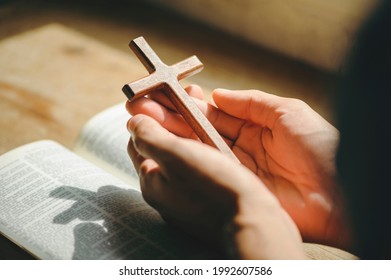 Man Pray For God Blessing To Wishing Have A Better Life. Man Hands Praying To God With The Bible And Cross. Believe In Goodness. Holding Hands In Prayer On A Wooden Table.