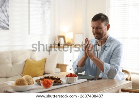 Man praying before dinner at table indoors. Space for text