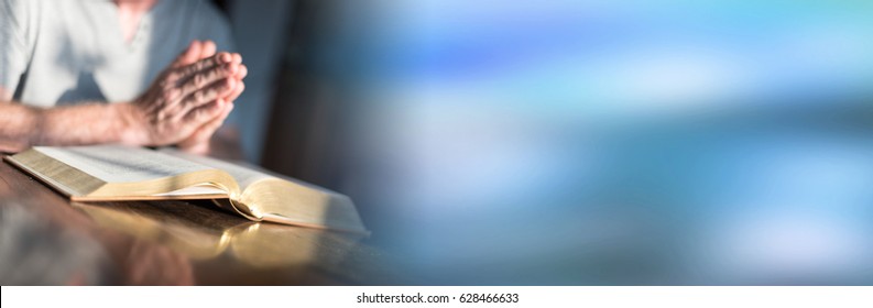 Man Praying With His Hands Over A Bible On Blurred Background