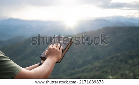 man praying on the holy bible in a field during beautiful sunset.male sitting with closed eyes with the Bible in his hands, Concept for faith, spirituality, and religion.