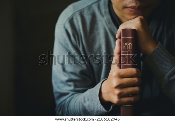 Man praying on the holy bible in the morning. Man\
hand with Bible praying, Hands folded in prayer on Holy Bible in\
church concept for faith, spirituality, religion.Christian life\
crisis prayer to god.