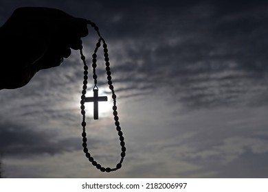 Man praying the rosary against black sky. Close-up. 