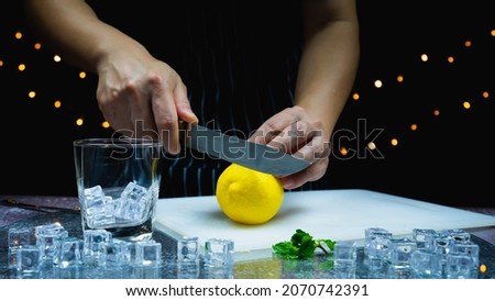 man prepare to cut fresh lemon on cutting board near leaf, ice, glass on table, bartender prepare fruit cocktail or fresh juice for drinking in party at bar