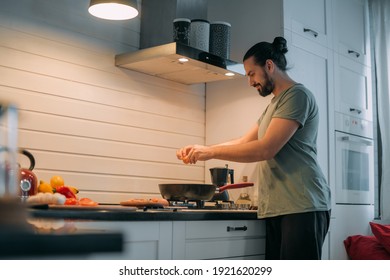 A man prepares breakfast in the kitchen. Young handsome caucasian male preparing food for himself for lunch on a gas stove in a large bright kitchen