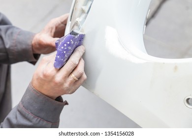 A Man Prepares A Car Body Element For Painting After An Accident With The Help Of Abrasive Paper In A Car Repair Shop. Recovery Bumper After A Collision.