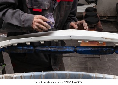 A Man Prepares A Car Body Element For Painting After An Accident With The Help Of Abrasive Paper In A Car Repair Shop. Recovery Bumper After A Collision.