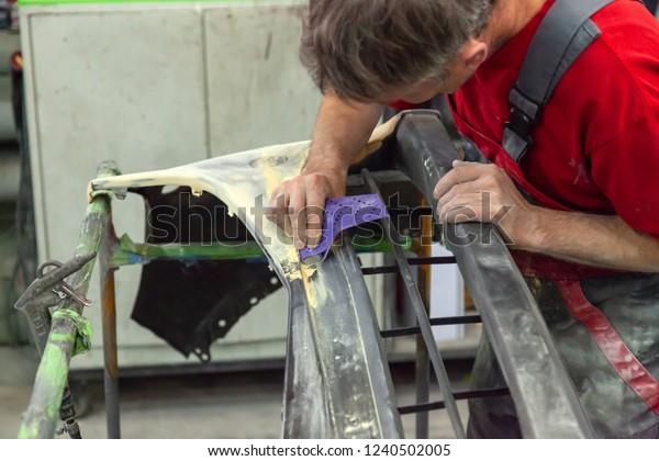 A man prepares a car body element for\
painting after an accident with the help of abrasive paper in a car\
repair shop. Recovery bumper after a\
collision.
