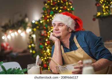 A Man Prepares Food In The Kitchen On Christmas Eve. A Dreamy Positive Young Adult Man. Merry Christmas And Happy Holidays. Decorated With Christmas Lights Interior.