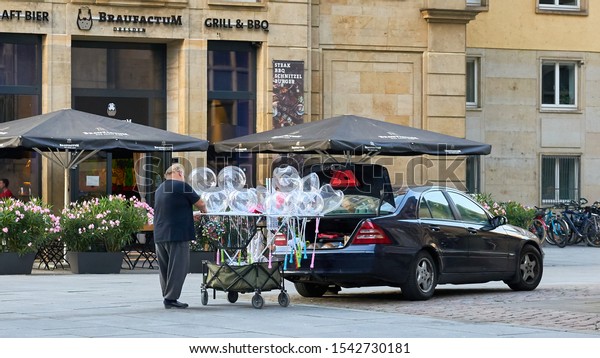 Man prepares glowing balloons for children from the back\
of his car on cobblestone street, for sale at the annual city\
festival in Dresden, Germany.  August 2019.                        \
   