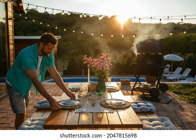 Man preparing a dinner table in the backyard. He is arranging and making final preparations for diner.