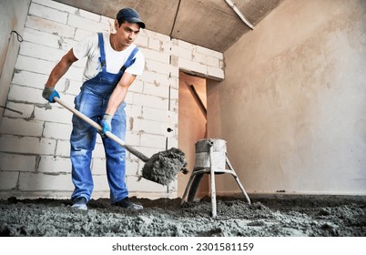 Man preparing floor screed material while standing near concrete screed mixer machine. Male worker using shovel while shoveling sand-cement mix in building under construction. - Powered by Shutterstock