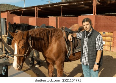 Man preparing horse for walk - putting on a saddle and bridle - Powered by Shutterstock